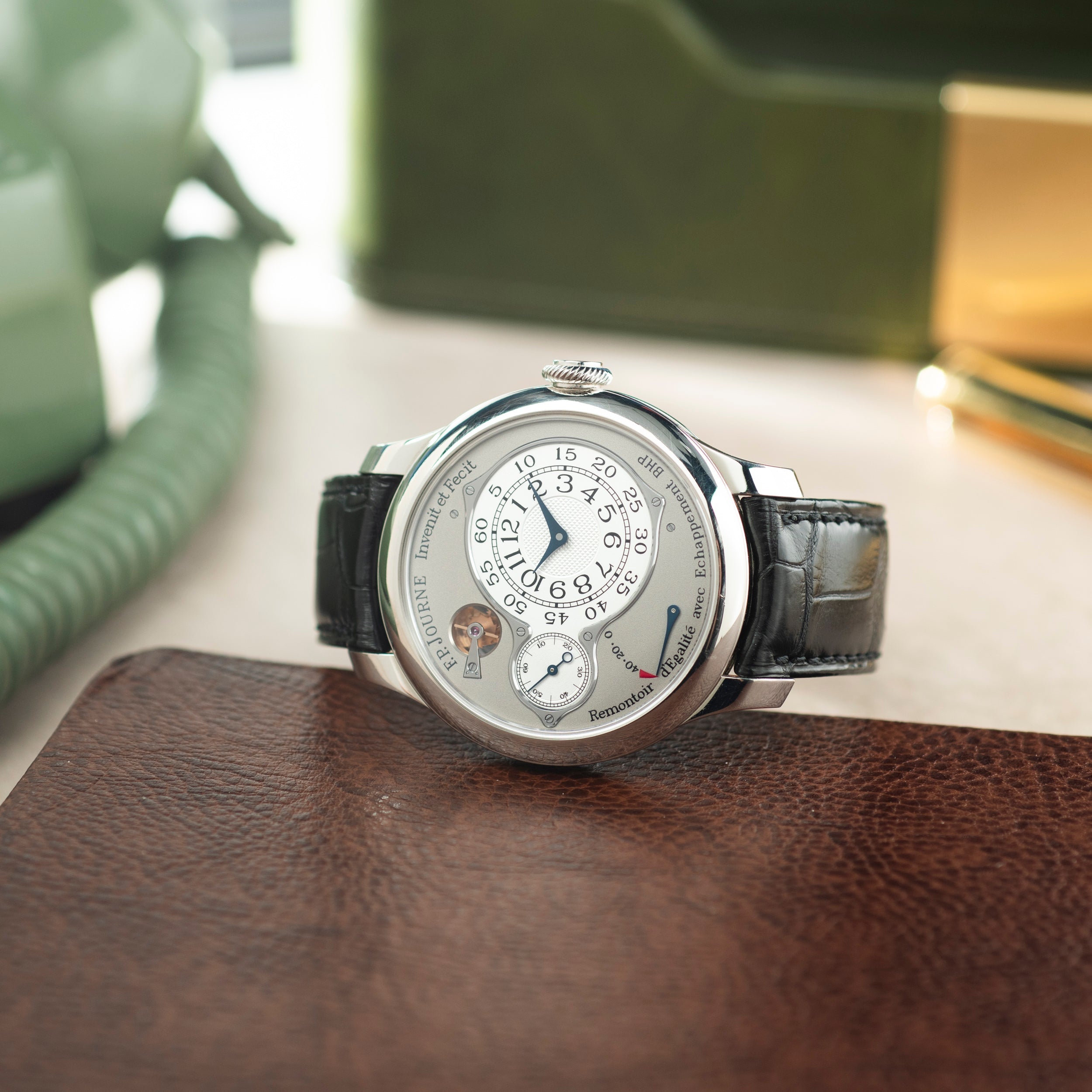 Silver-toned round watch with white dial, circular time display, black leather strap, displayed on brown leather surface.