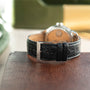 Silver-tone watch with tan dial, black crocodile leather strap, and F.P. Journe branding on clasp, displayed caseback-up.