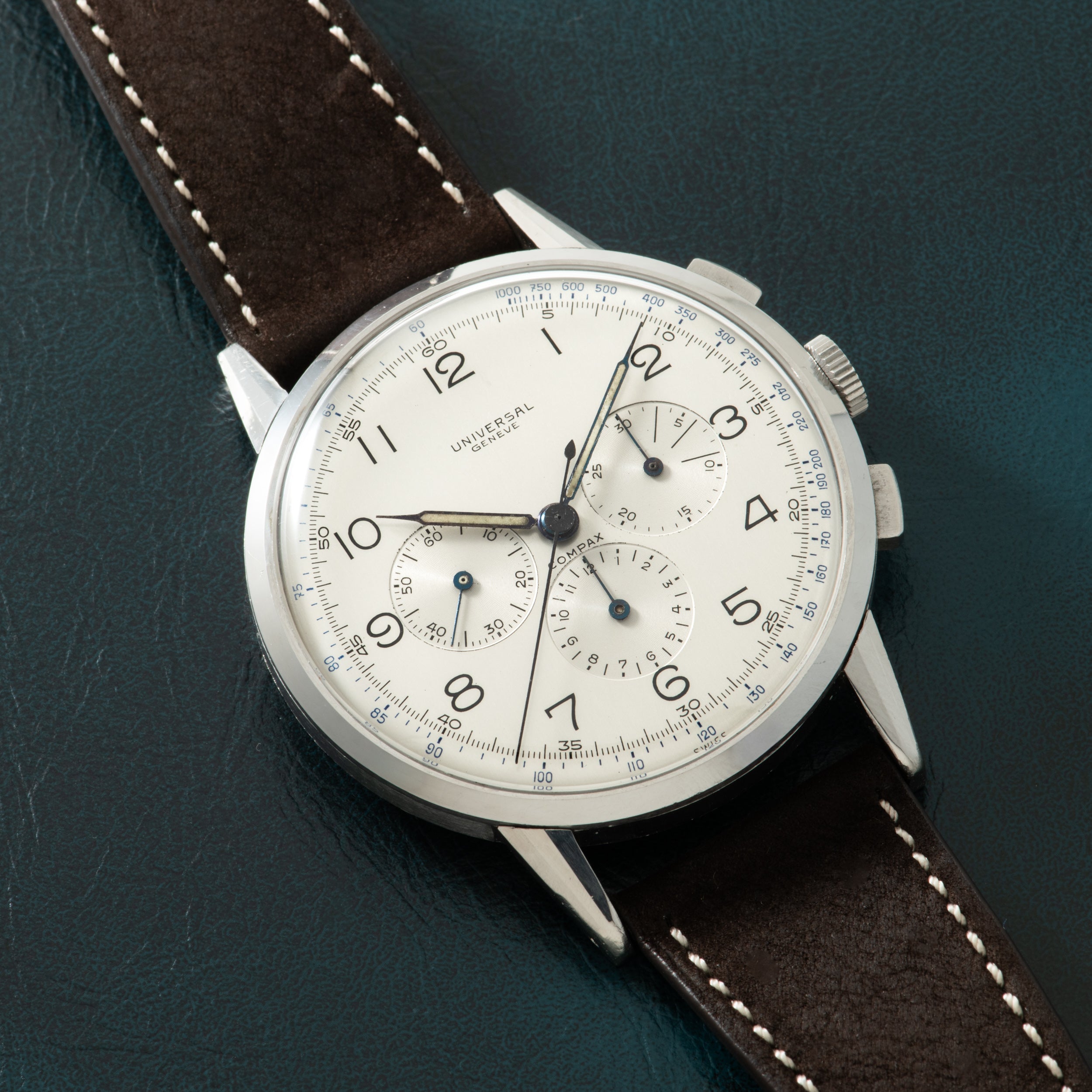 Silver-cased chronograph watch with cream dial, Arabic numerals, two subdials, and dark brown leather strap with white stitch