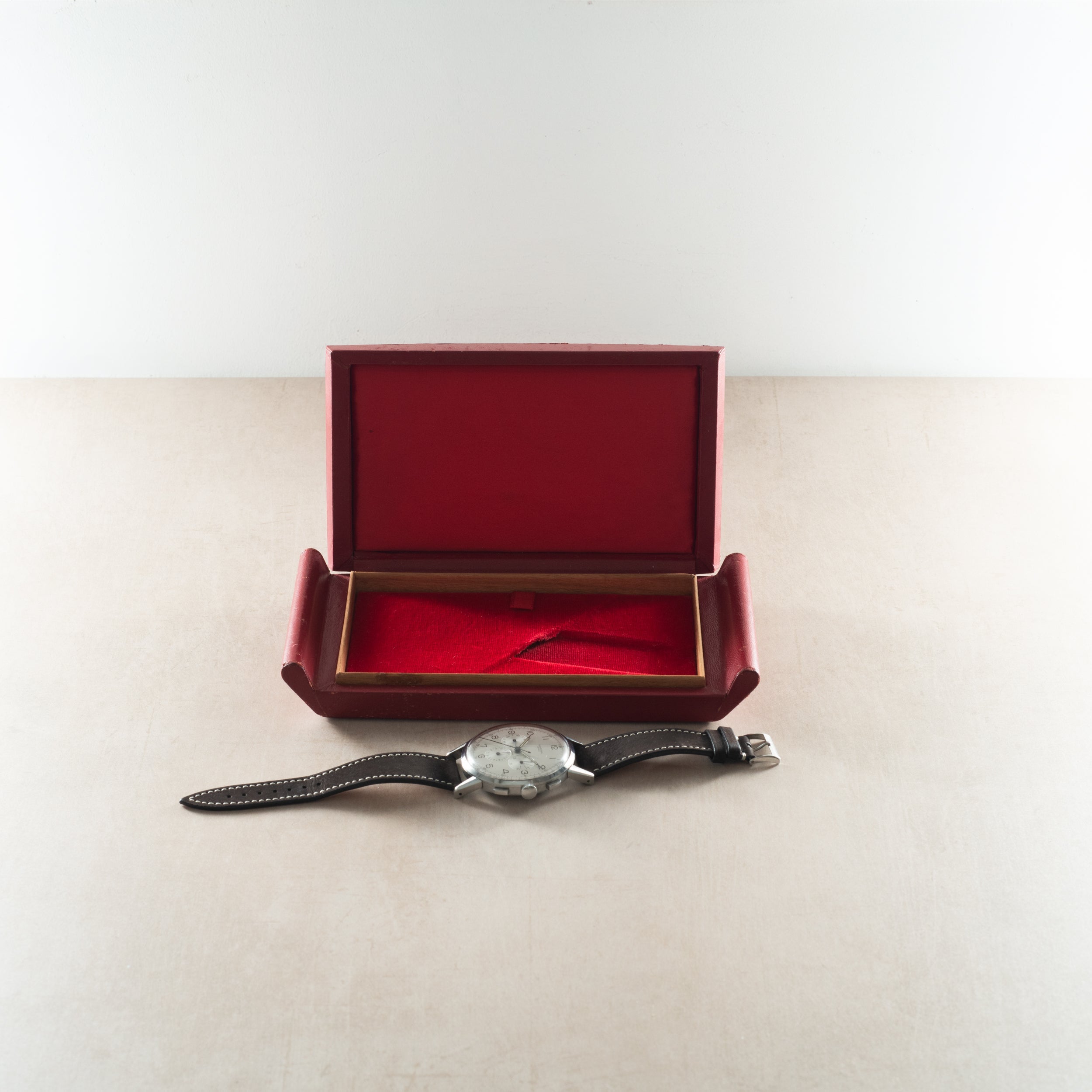 Chronograph watch with silver dial and black leather strap displayed with open burgundy presentation box.
