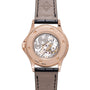 Rose gold watch with exposed mechanical movement visible through case back, black leather strap with cross emblem.