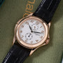 Rose gold watch with white dial, Arabic numerals, two subdials, and black leather strap on green fabric background.