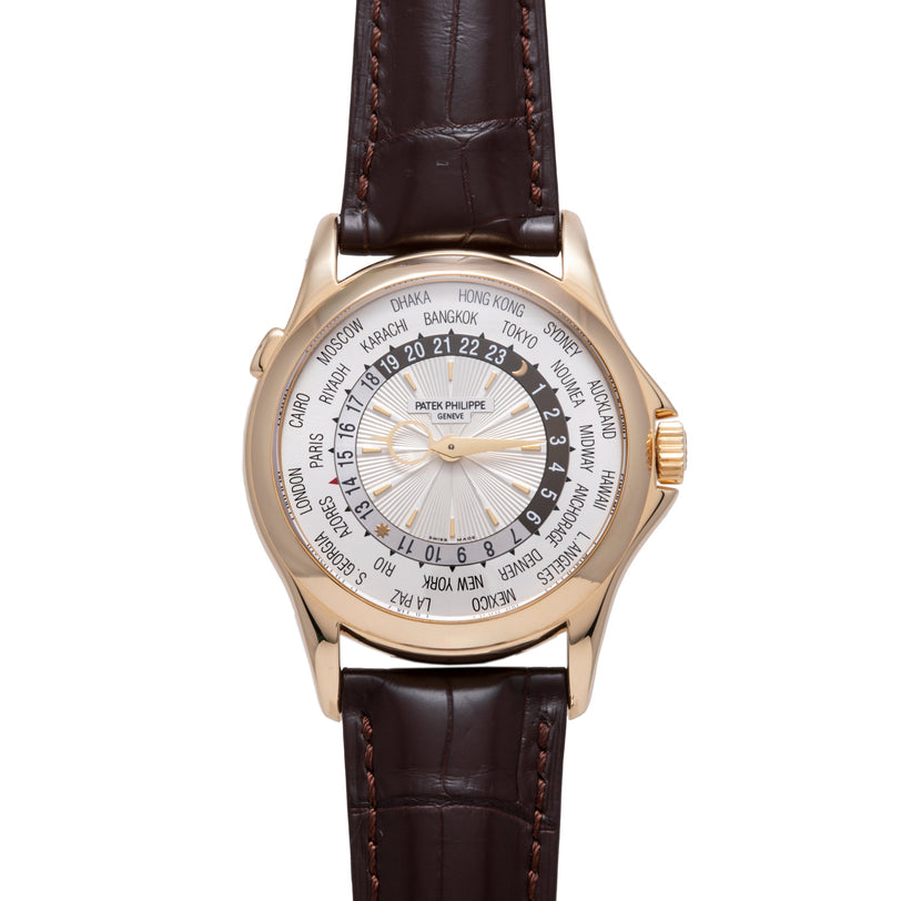 Rose gold watch with white dial displaying world city time zones, dark brown leather strap with stitching.