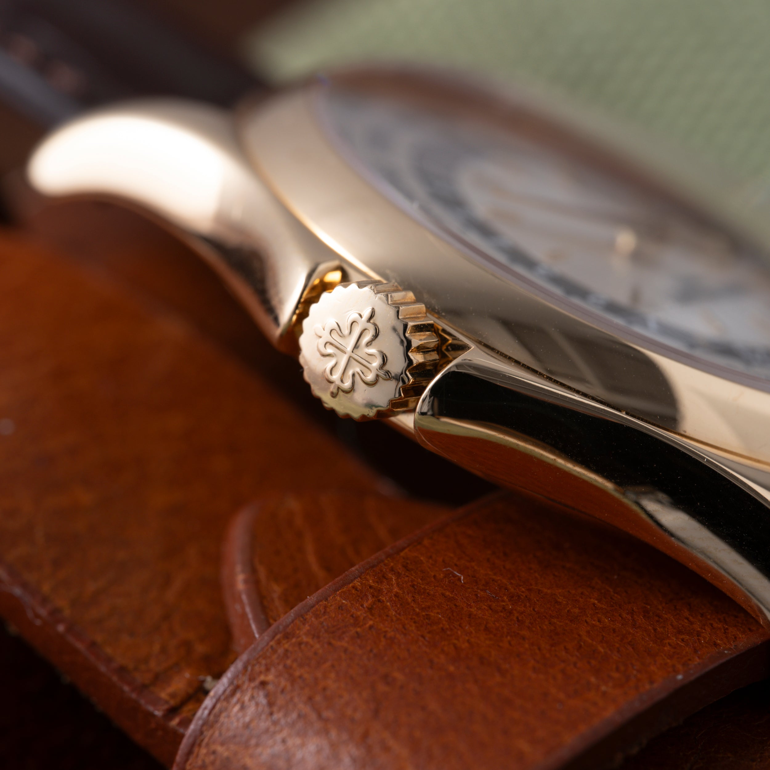 Luxury watch with silver case and brown leather strap, crown detail visible, resting on wooden surface.