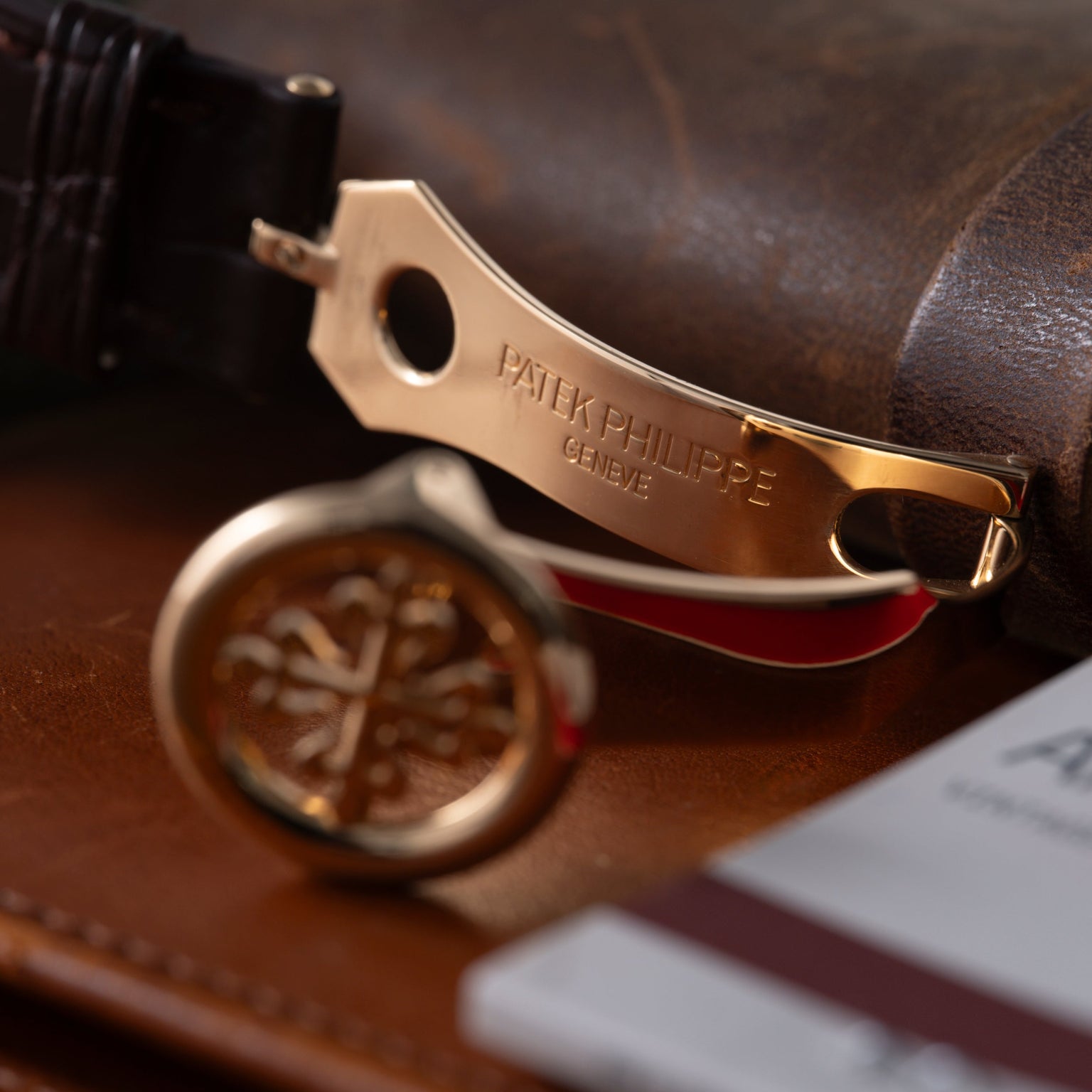 Gold-tone Patek Philippe watch with black leather strap resting on brown leather surface.
