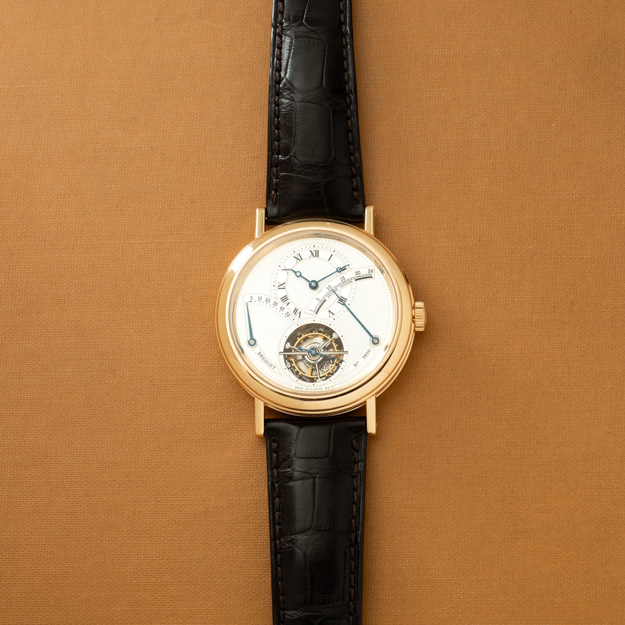 Gold-tone watch with white dial, Roman numerals, black crocodile leather strap, and visible tourbillon mechanism at bottom.
