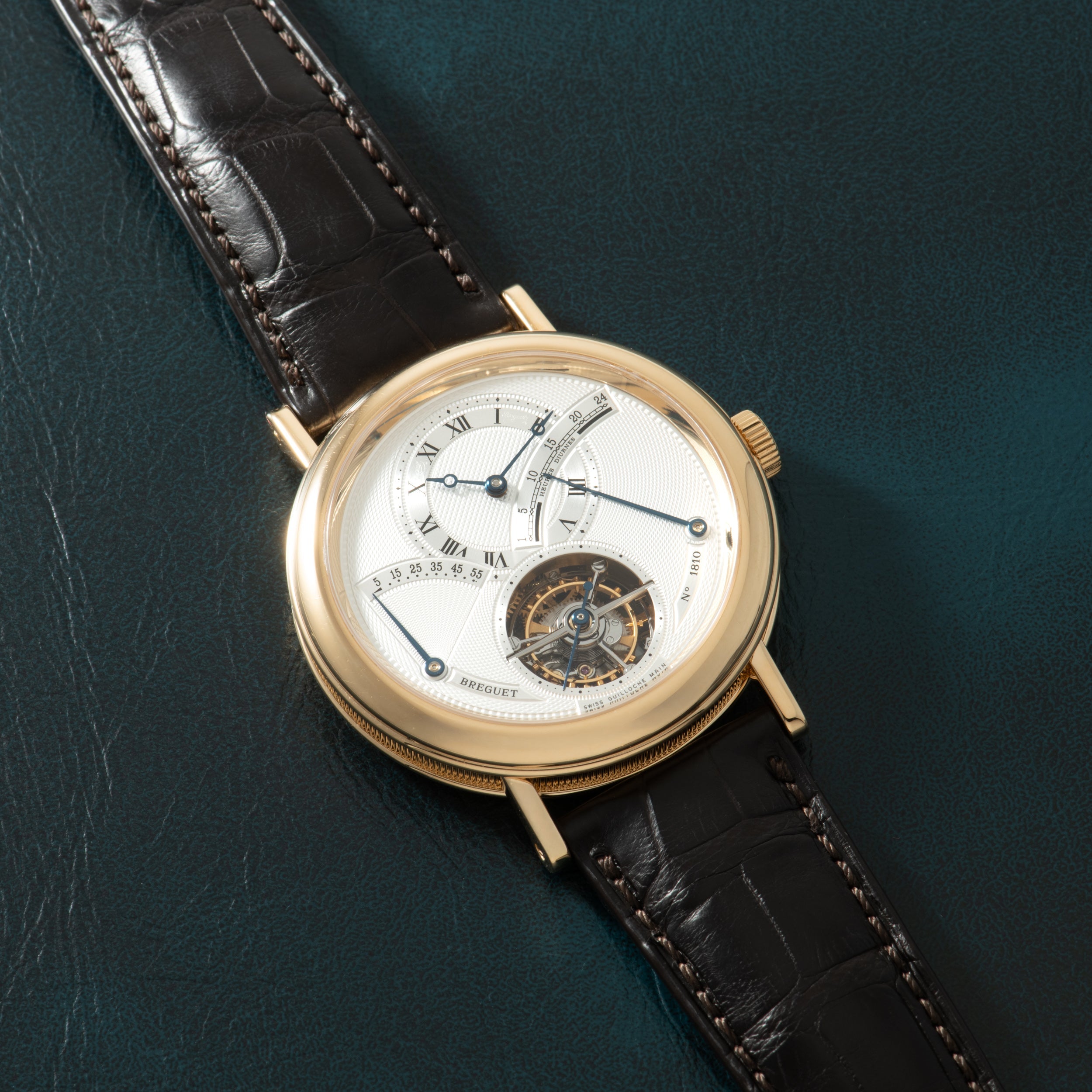 Gold-tone watch with white dial featuring Roman numerals, visible tourbillon mechanism, and black leather crocodile-embossed