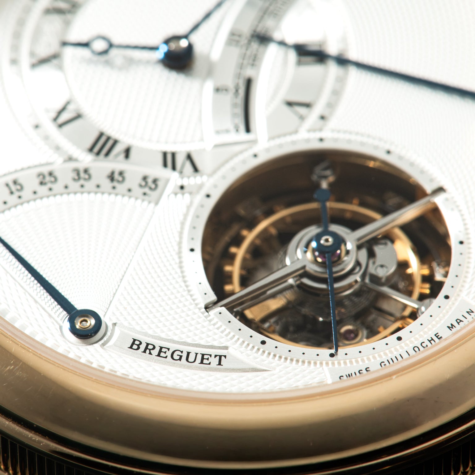 Luxury watch with cream dial, Roman numerals, blue hands, visible tourbillon mechanism in circular aperture, and gold-tone ca