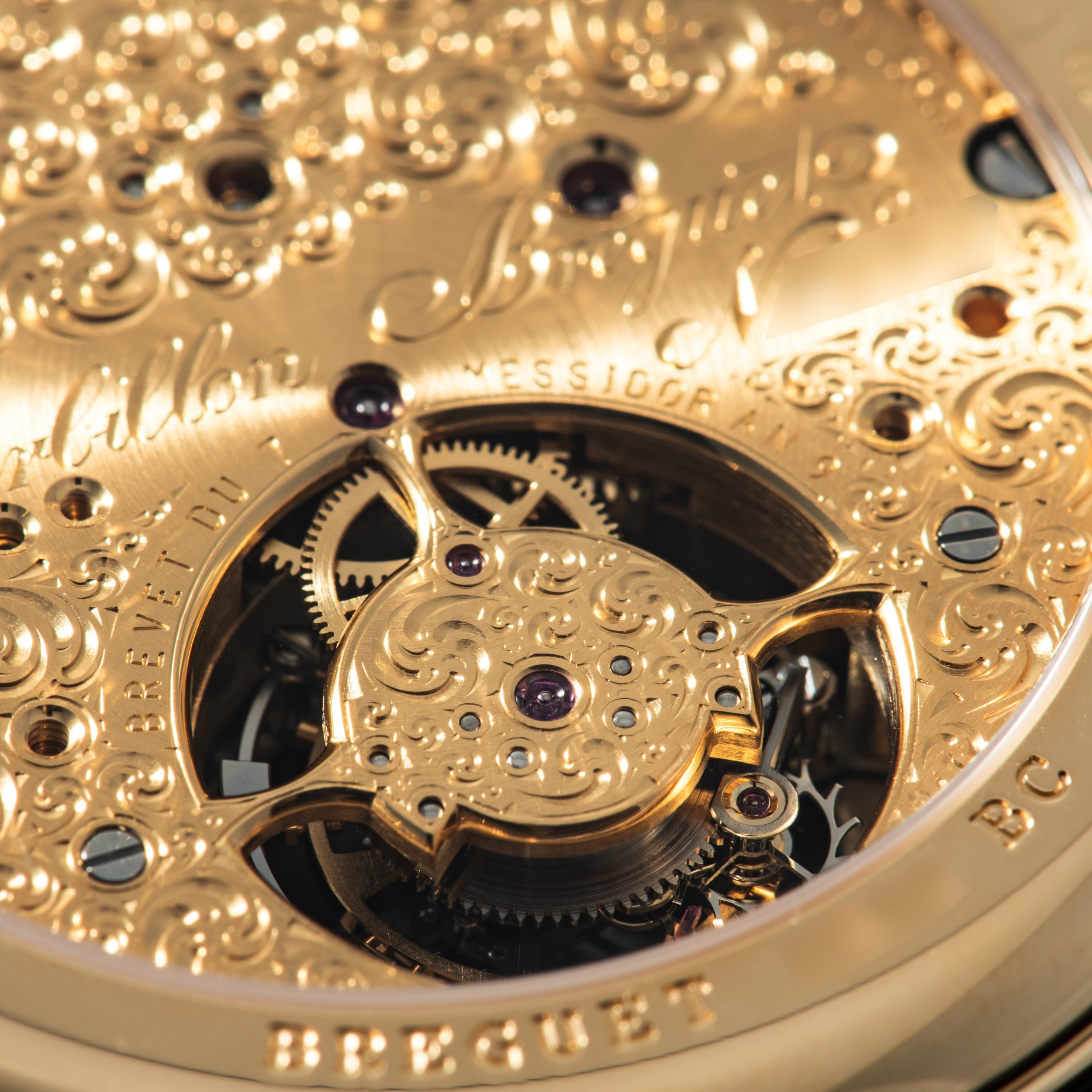 Gold watch movement with ornate engraved plate, visible tourbillon cage, jeweled bearings, and mechanical gears through displ