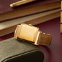 Gold-tone rectangular watch with cream dial and brown leather strap on fabric surface.