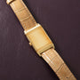 Gold-tone rectangular watch with cream dial and tan crocodile leather strap on dark background.