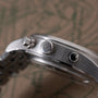 Stainless steel pilot's chronograph watch with brushed case, crown, and subdials visible from the side angle.
