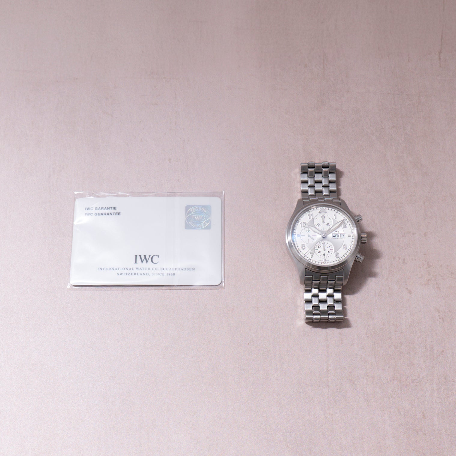 IWC Pilot's Chronograph Spitfire with stainless steel bracelet and white dial, displayed with warranty card.