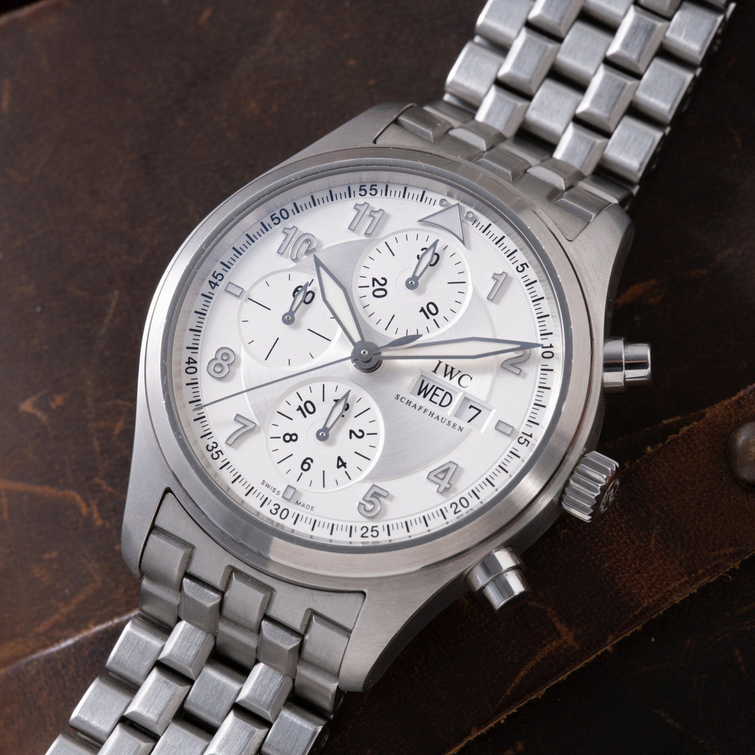 Stainless steel chronograph watch with white dial, three subdials, Arabic numerals, and matching steel bracelet on brown leat