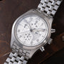 Stainless steel chronograph watch with white dial, three subdials, Arabic numerals, and matching steel bracelet on brown leat