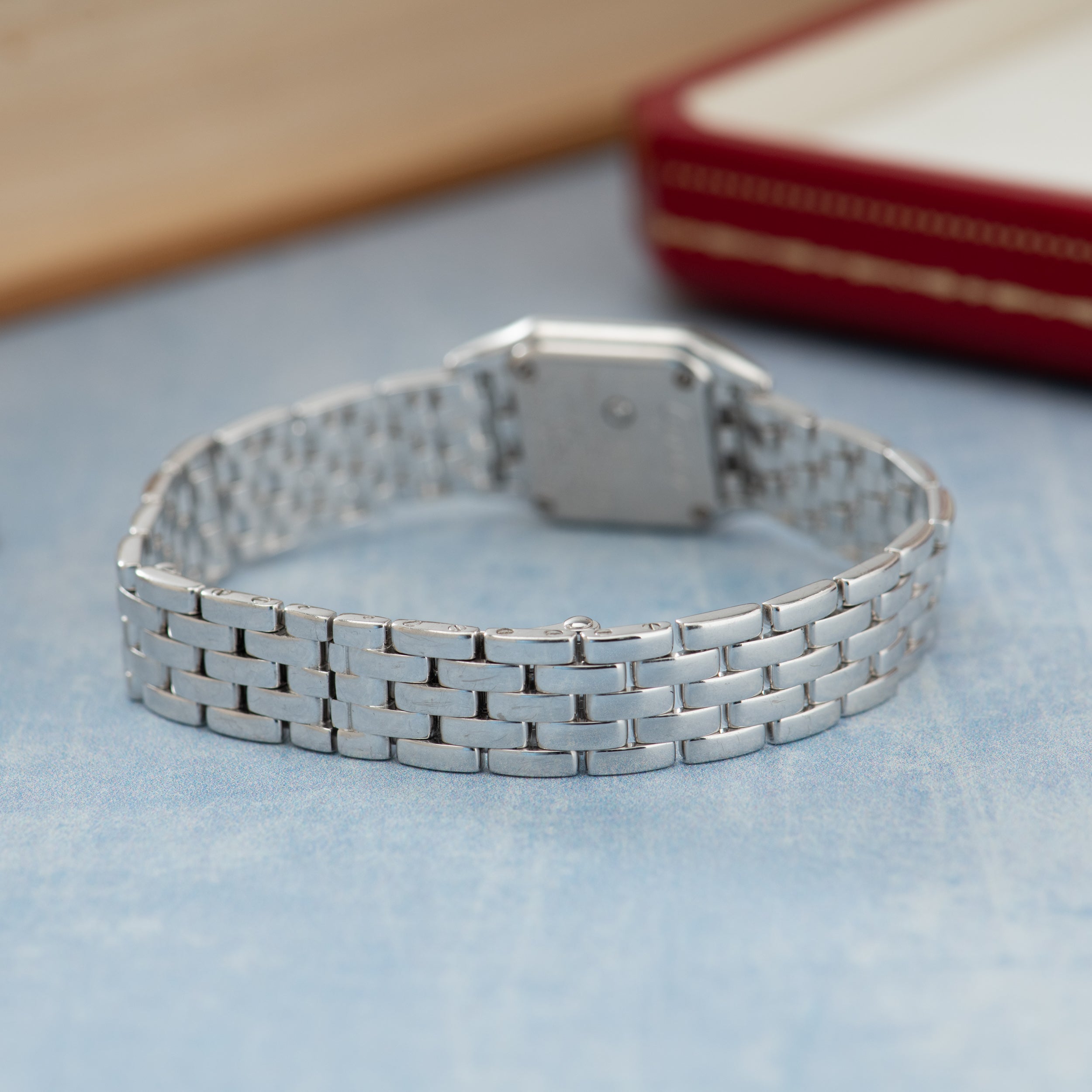 Silver-tone rectangular watch with linked metal bracelet band displayed on light blue surface.