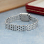 Silver-tone rectangular watch with linked metal bracelet band displayed on light blue surface.