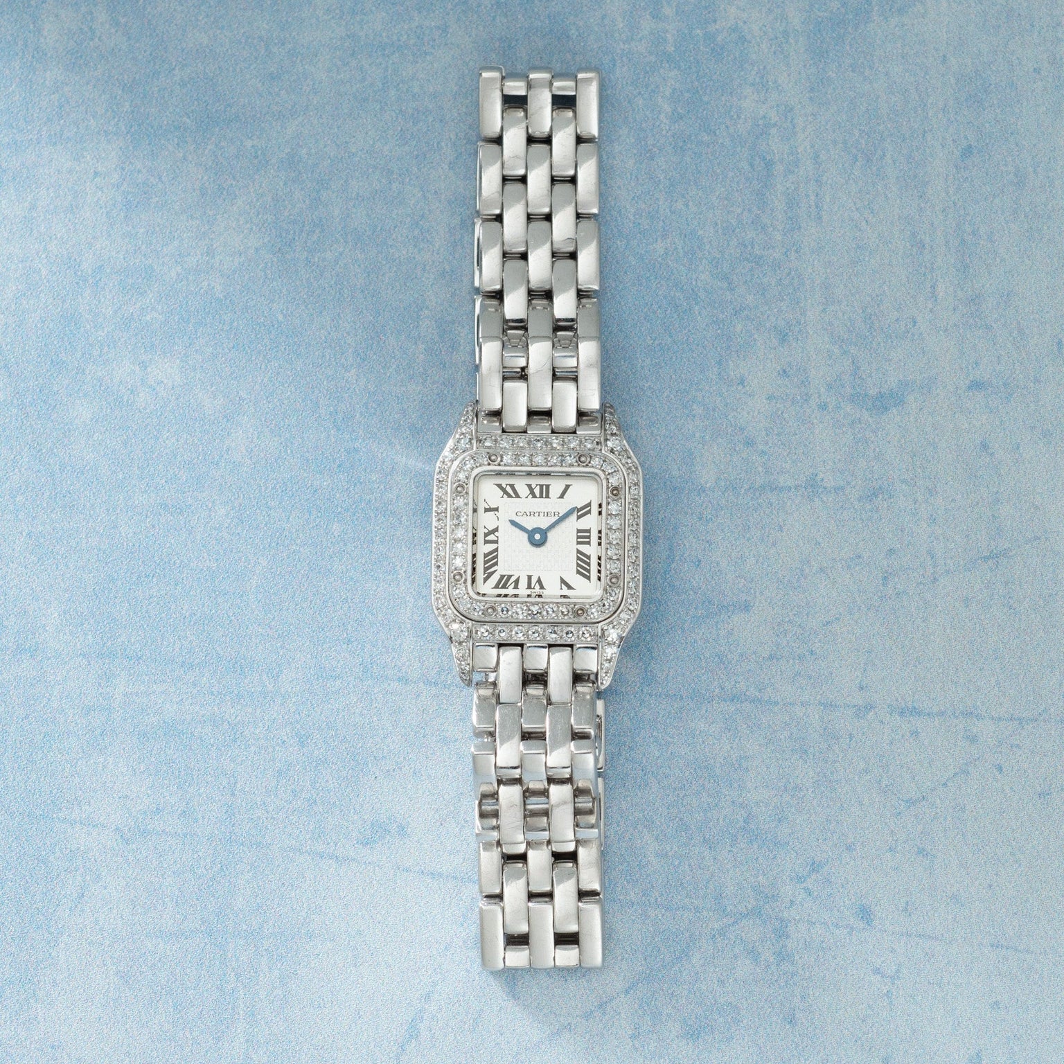 Stainless steel rectangular watch with diamond-set bezel, cream dial with Roman numerals, blue hands, and multi-link metal br