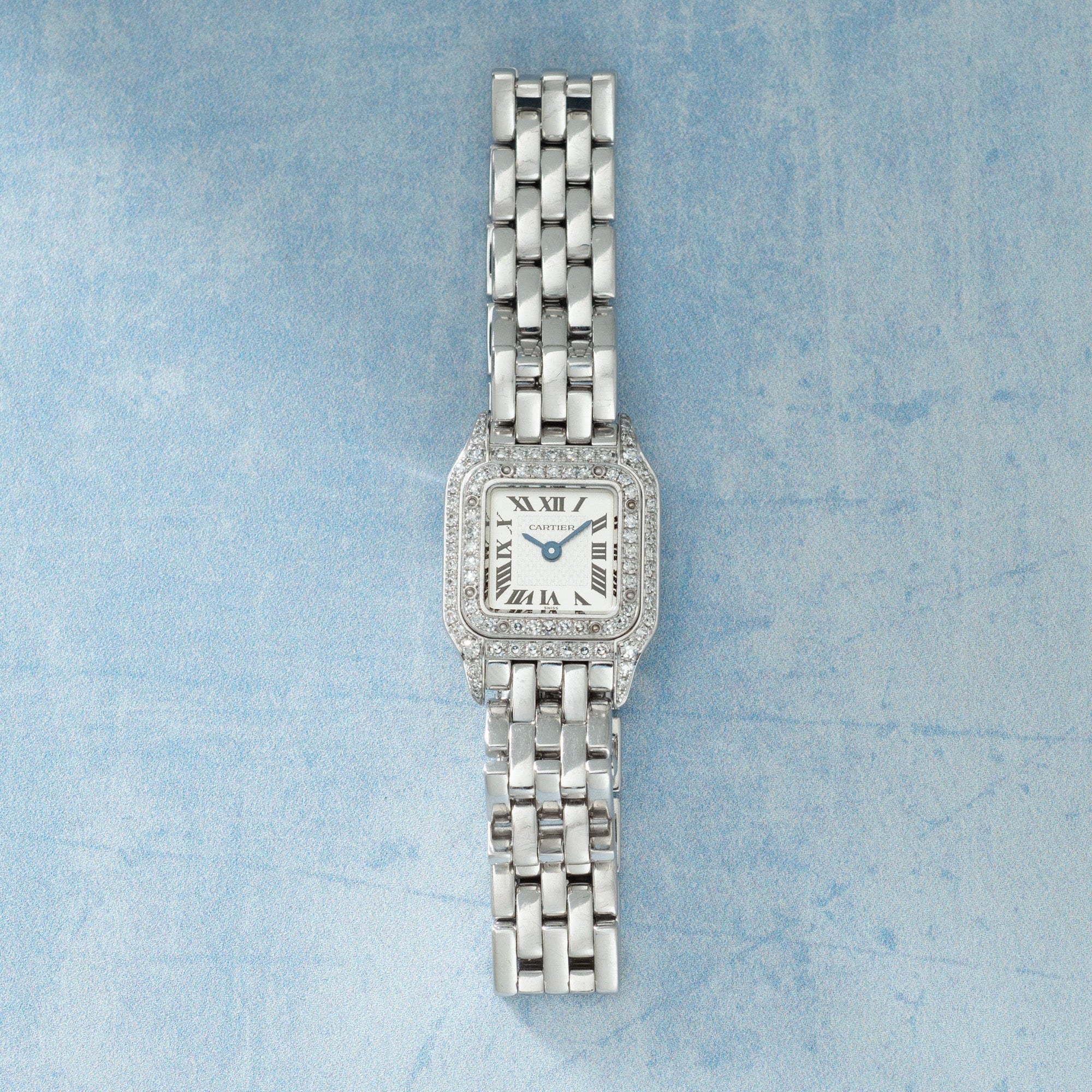 Stainless steel rectangular watch with diamond-set bezel, cream dial with Roman numerals, blue hands, and multi-link metal br