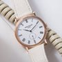 Rose gold Patek Philippe Calatrava watch with white dial, Roman numerals, and cream leather strap.