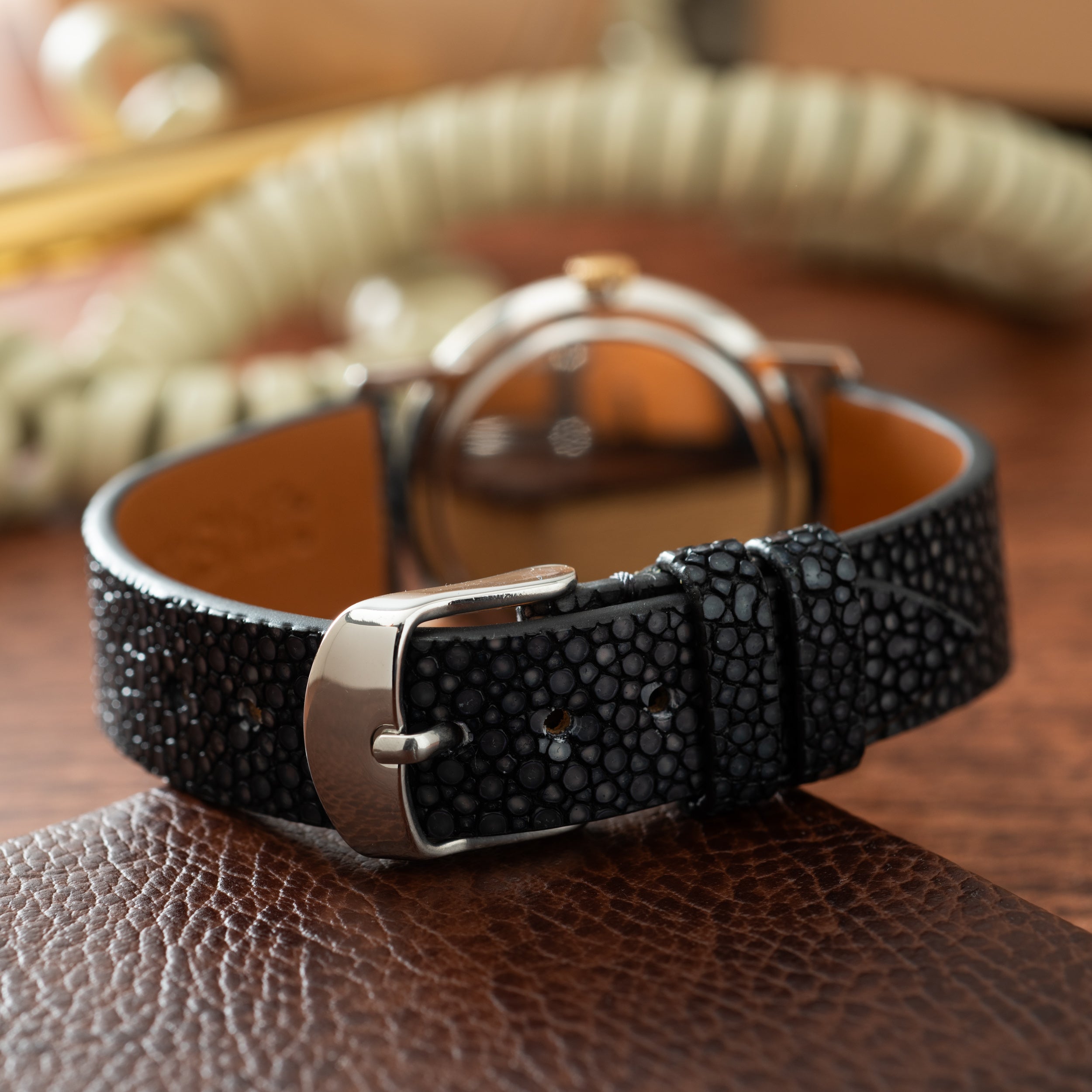 Black textured leather strap watch with silver-tone case and tan dial displayed on brown surface.