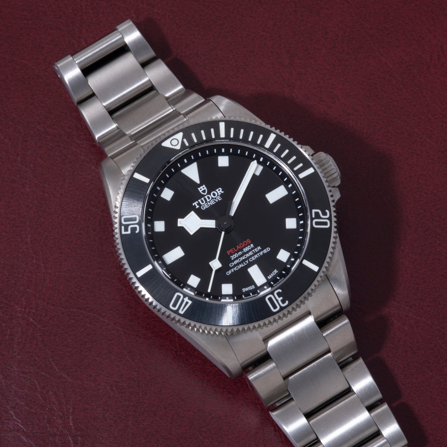 Stainless steel dive watch with black dial, white hour markers, rotating bezel, and metal bracelet on burgundy background.