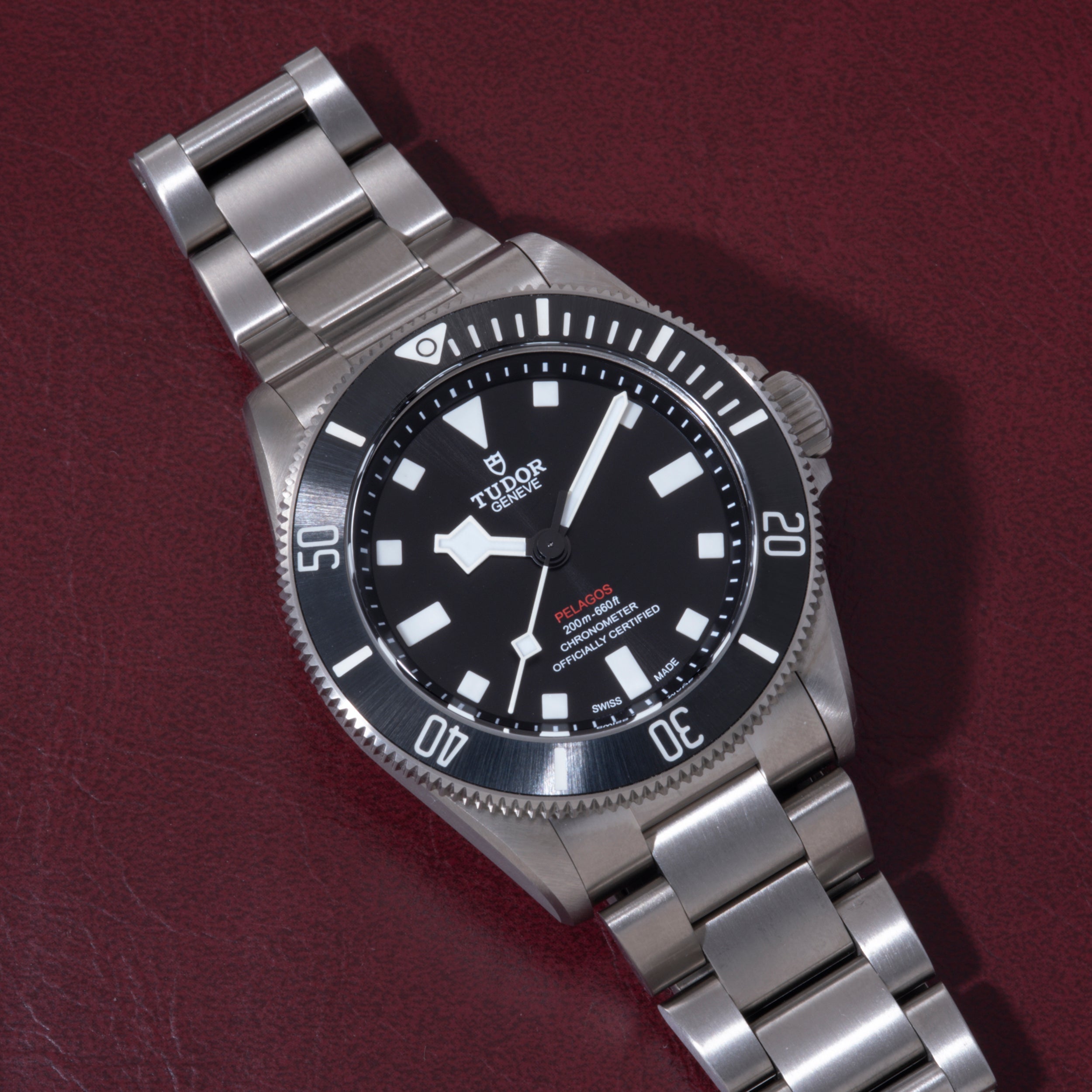 Stainless steel dive watch with black dial, white hour markers, rotating bezel, and metal bracelet on burgundy background.