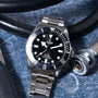 Tudor Pelagos 39 dive watch with stainless steel bracelet and black dial on blue textured surface with diving equipment.