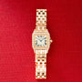 Rose gold watch with square face, diamond-set bezel, Roman numeral dial, and linked bracelet on red background.