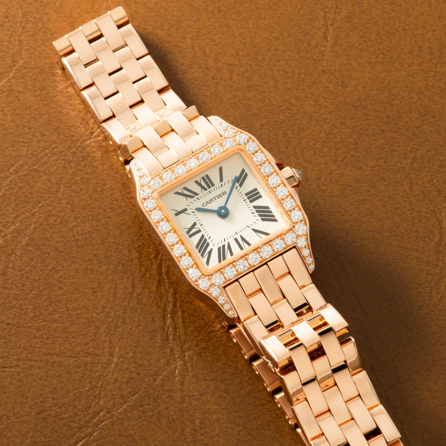 Rose gold square watch with diamond-set bezel, cream dial, Roman numerals, and matching link bracelet on tan leather backgrou