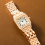 Rose gold square watch with diamond-set bezel, cream dial, Roman numerals, and matching link bracelet on tan leather backgrou