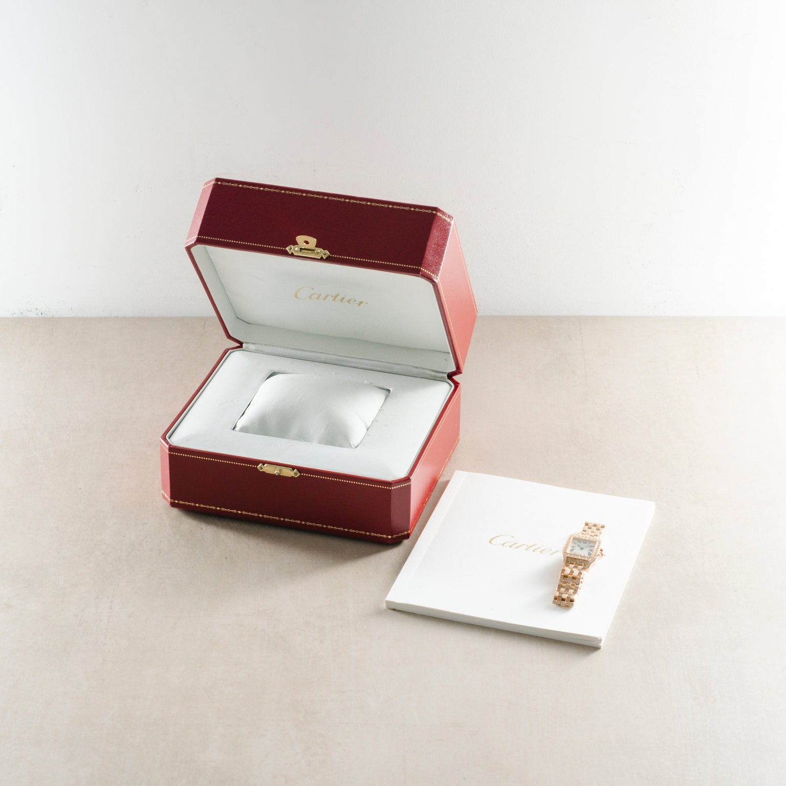 Rose gold rectangular wristwatch with diamond bezel displayed in burgundy Cartier box and on white card.