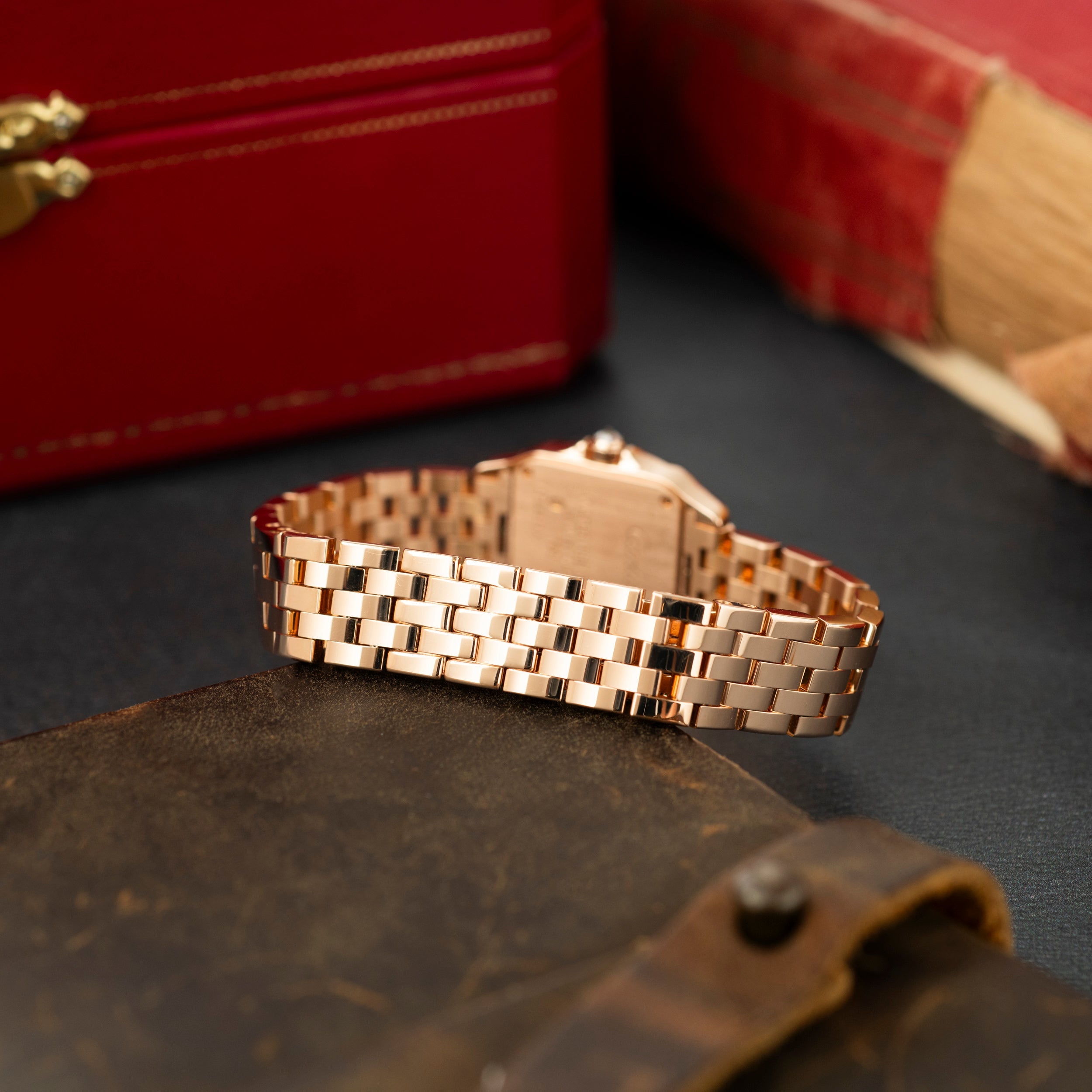 Rose gold rectangular watch with linked bracelet band, displayed on dark surface with red box in background.