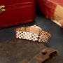 Rose gold rectangular watch with linked bracelet band, displayed on dark surface with red box in background.