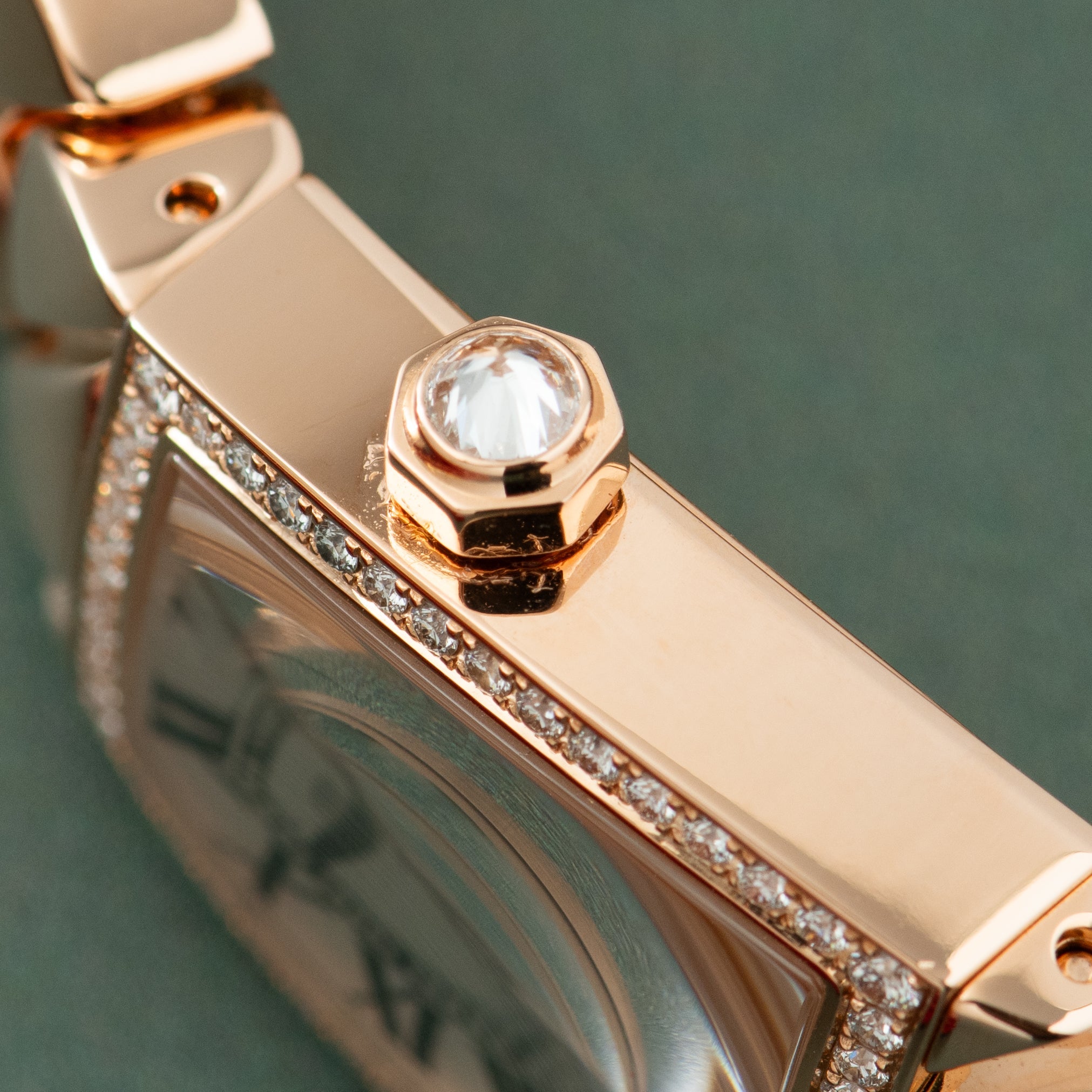 Rose gold watch with crystal crown and diamond-set bezel on pale green background.