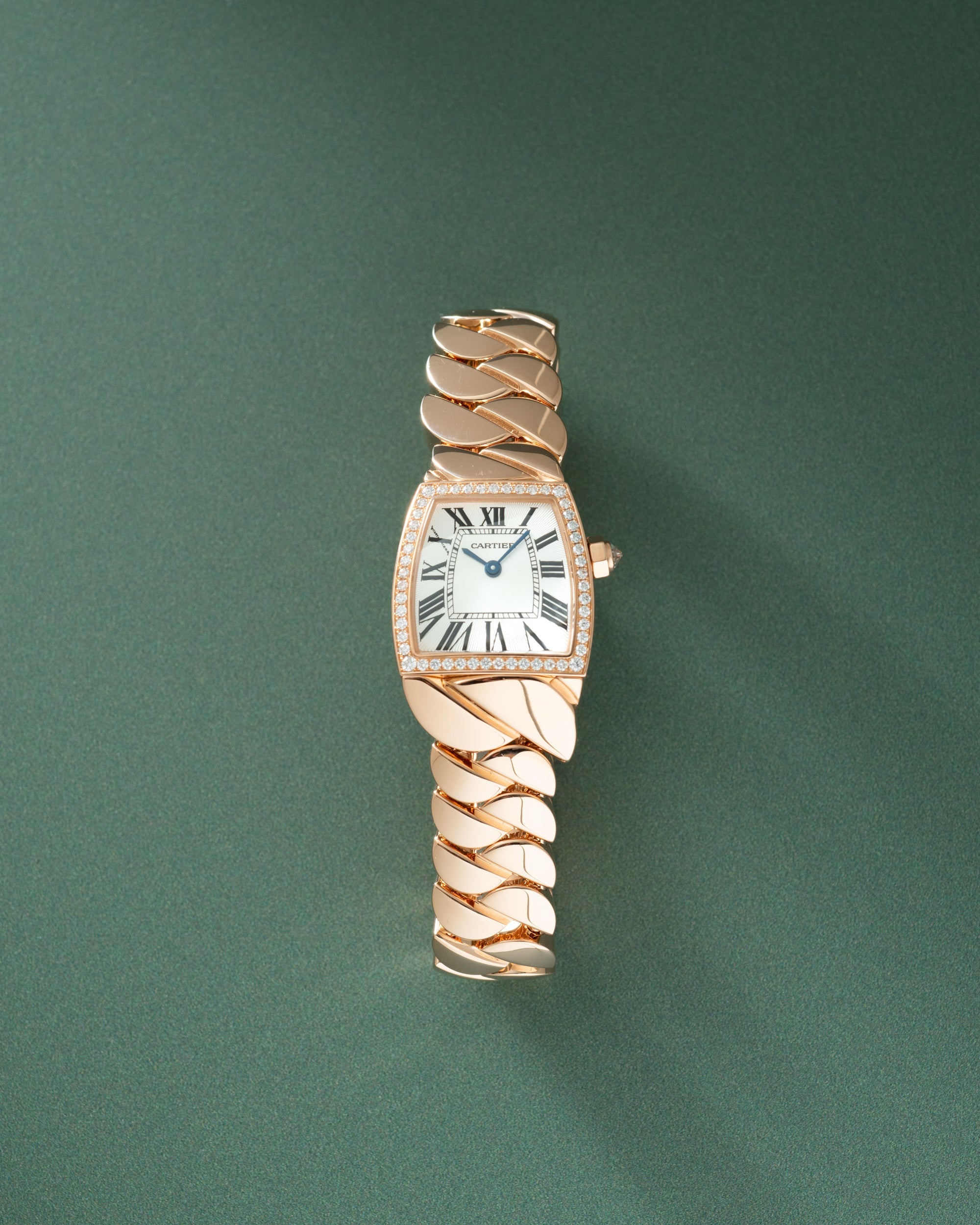Rose gold watch with rectangular white dial, Roman numerals, diamond-set bezel, and intertwined rose gold bracelet against gr