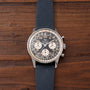 Breitling Cosmonaute chronograph watch with black dial, white subdials, and blue fabric strap on wooden surface.
