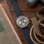 Breitling Cosmonaute chronograph watch with dark blue dial, white subdials, and navy fabric strap on wooden surface.