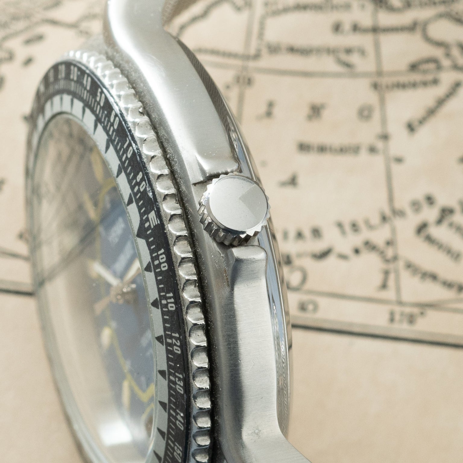 Silver watch with black bezel and textured dial, shown from side angle on a map background.