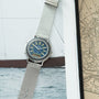 Yema Spationaute ISS watch with blue dial and metal mesh band, displayed on nautical chart and ocean photograph.