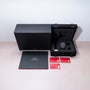 Omega Speedmaster watch with chronograph dial in black case, displayed with black presentation box, gray documentation folder