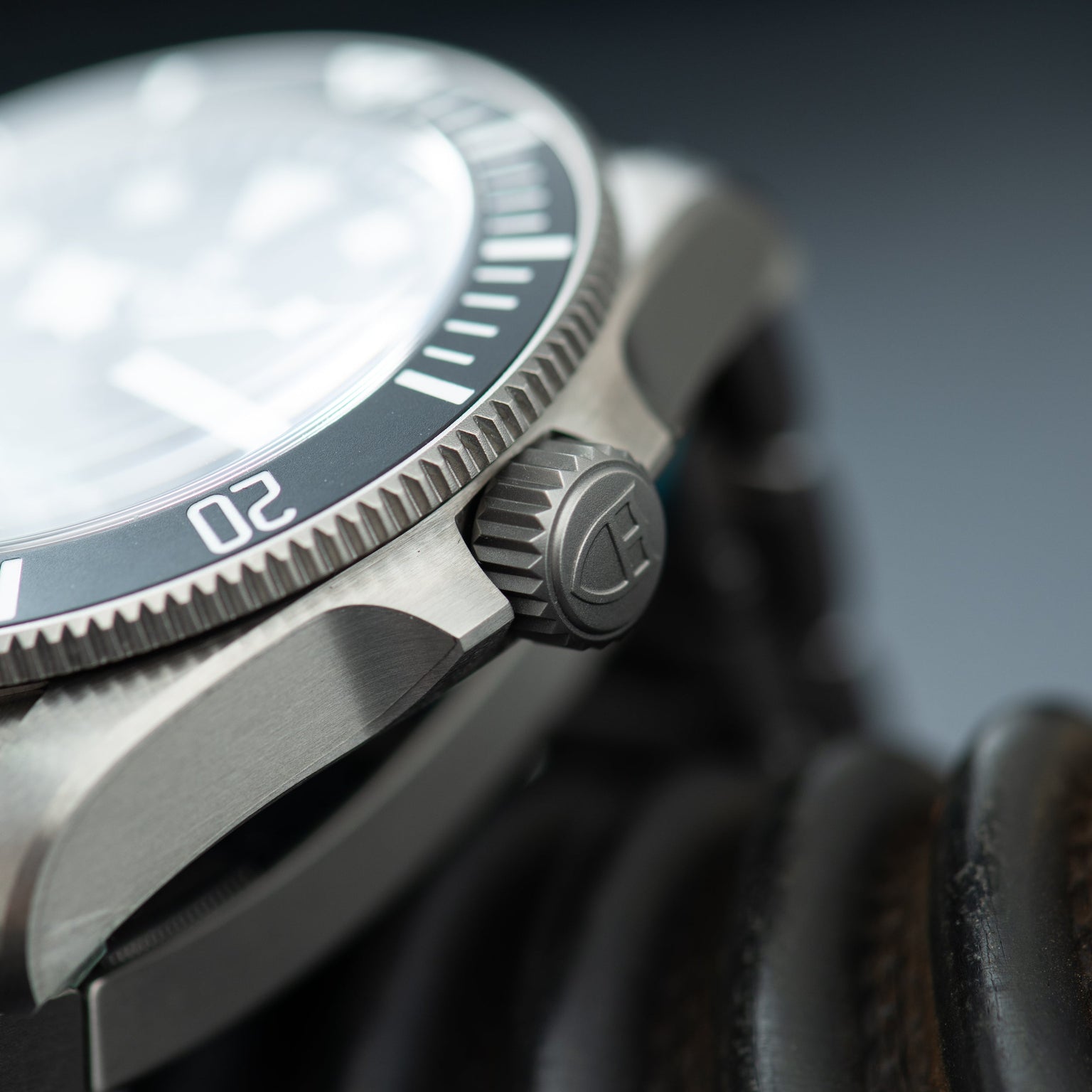 Steel dive watch with white dial, dark rotating bezel, and textured crown detail shown from side angle.