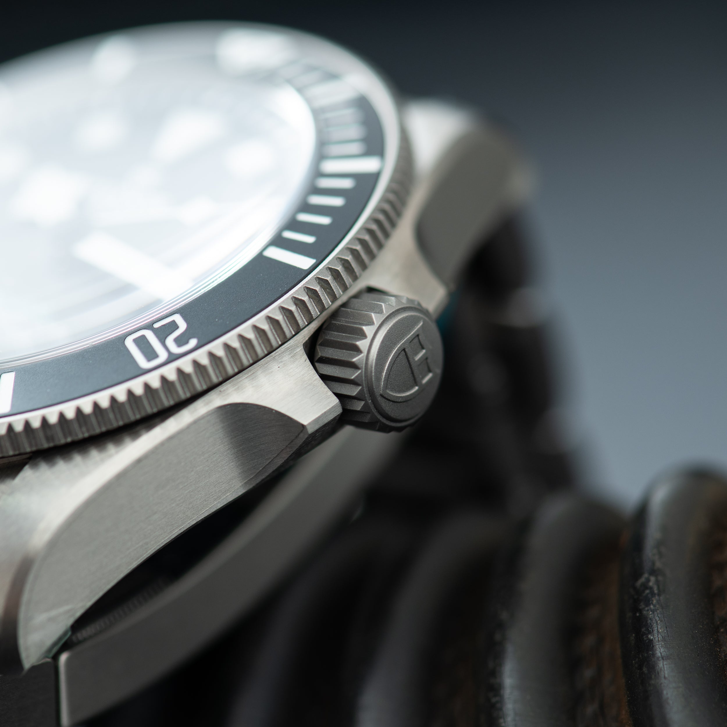 Steel dive watch with white dial, dark rotating bezel, and textured crown detail shown from side angle.