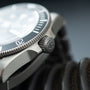 Steel dive watch with white dial, dark rotating bezel, and textured crown detail shown from side angle.