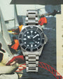 Tudor Pelagos Ultra stainless steel watch with black dial, white hour markers, date window, and metal bracelet.