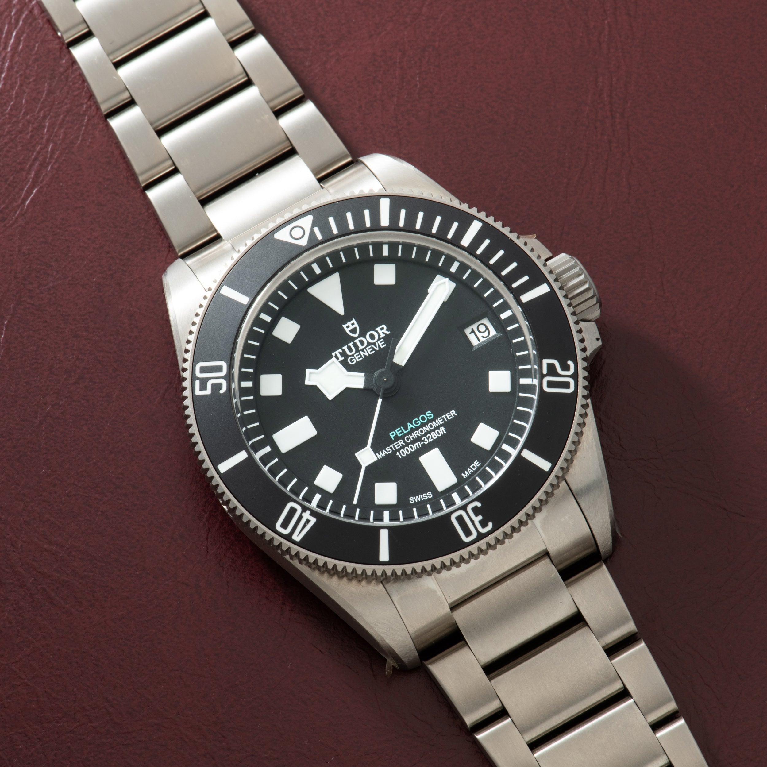 Steel dive watch with black dial, white hour markers, rotating bezel, and three-link bracelet on burgundy background.