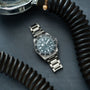 Tudor Pelagos Ultra dive watch with dark dial and stainless steel bracelet, displayed on blue surface surrounded by black coi