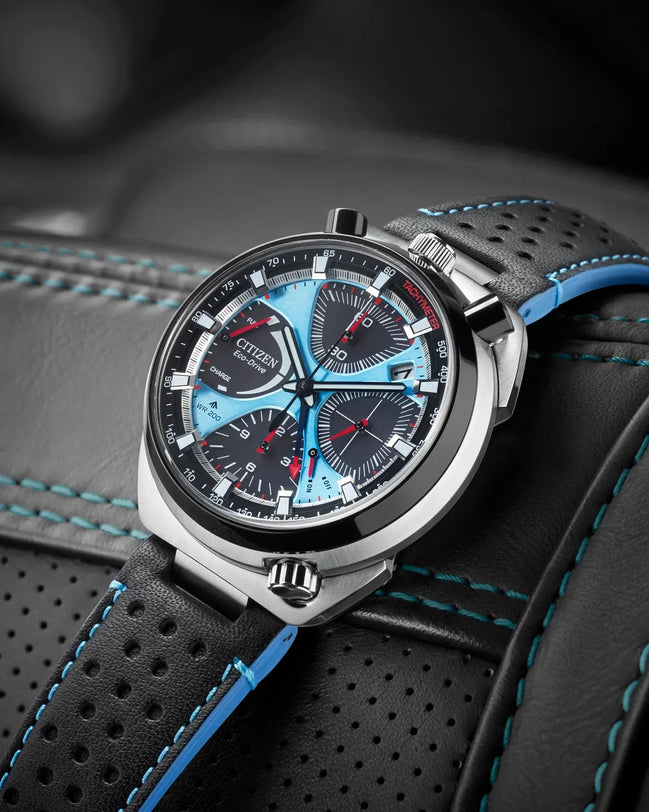 Blue and black chronograph watch with metal case on black leather strap with blue stitching and perforations.