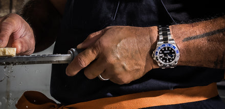 Person grating cheese, wearing a watch with a blue and black face