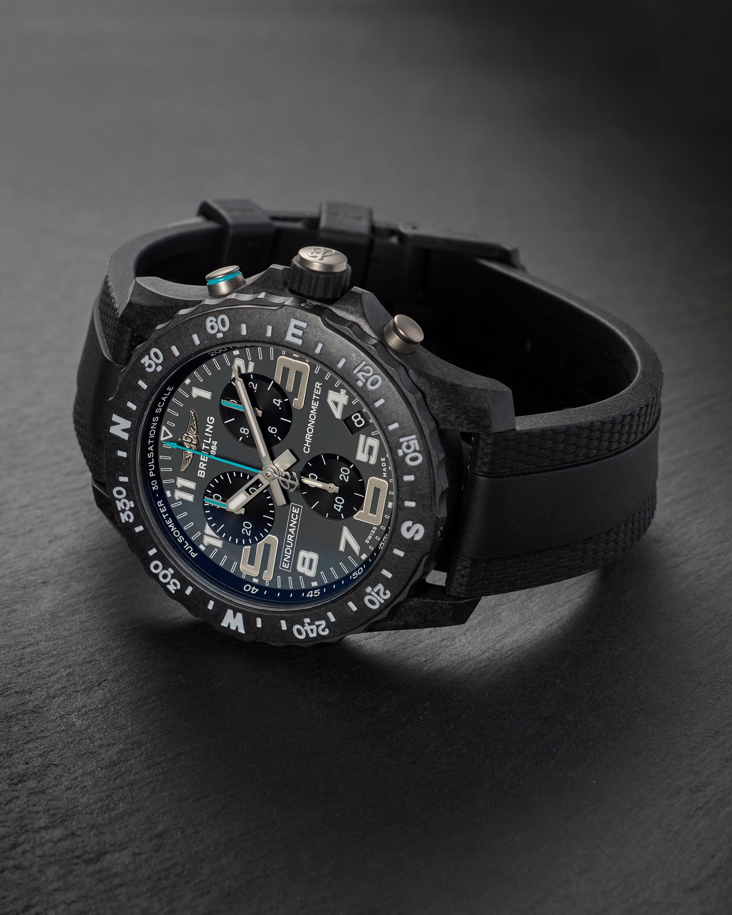 Black Breitling chronograph watch with black rubber strap on a dark surface.
